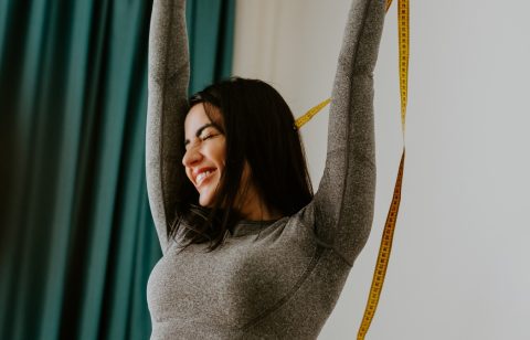happy Woman Measuring body With Tape after weight loss fitness workout. Beautiful smiling woman measuring butt in front of mirror in living room after fitness marathon