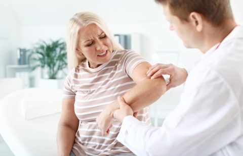 Doctor examining mature woman with joint pain in clinic